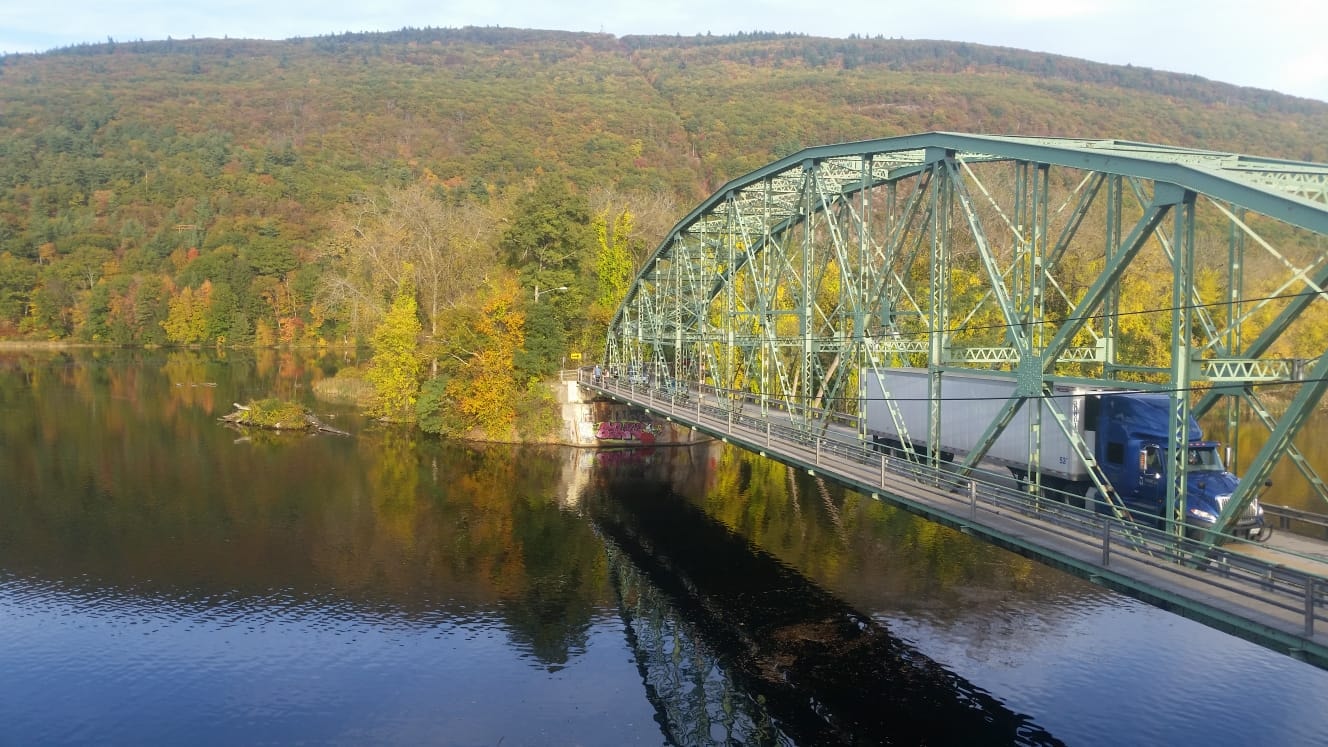 Steel bridge crossing a reflective Vermont river in autumn